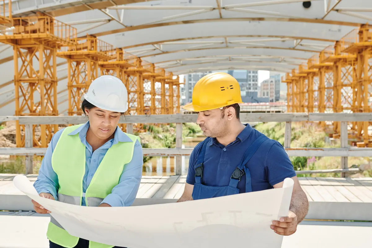 Two people in hard hats reviewing building plans at a job site